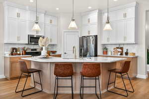 Kitchen featuring tasteful backsplash, a kitchen island with sink, stainless steel appliances, hanging light fixtures, and two tone color scheme