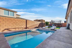 View of pool with a fenced backyard, patio surround, and a trampoline