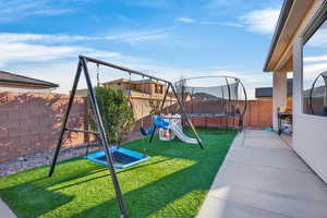 View of jungle gym with a trampoline, a fenced backyard, and a patio area