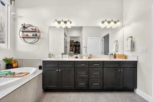Primary ensuite bathroom featuring double vanity, a spacious closet, a bath, a shower stall, and light tile patterned floors