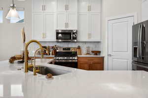 Kitchen featuring stainless steel appliances, light stone countertops, decorative light fixtures, and white cabinets