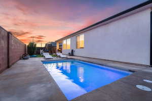 Pool at dusk with a fenced backyard and a covered patio area