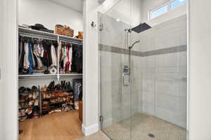 Primary ensuite bathroom featuring a walk in closet, a stall shower, and wood finished floors