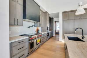Kitchen featuring stainless steel appliances, light wood-type flooring, extractor fan, gray cabinetry, and light stone countertops