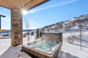 Yard covered in snow featuring a mountain view, a hot tub, and a patio area