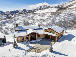 View of front facade featuring stone siding, a chimney, a mountain view, concrete driveway, and an attached garage