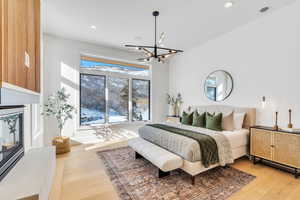 Bedroom with a glass covered fireplace, light wood-style flooring, and suspended lighting