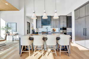 Kitchen with gray cabinets, a kitchen bar, pendant lighting, a center island with sink, and light wood-style floors