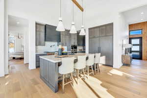 Kitchen featuring pendant lighting, a breakfast bar area, light wood-type flooring, gray cabinets, and a high ceiling