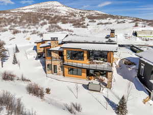 Snow covered rear of property with a chimney, stone siding, a patio, and a mountain view