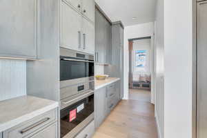 Kitchen with stainless steel double oven, light countertops, gray cabinetry, and light wood-type flooring