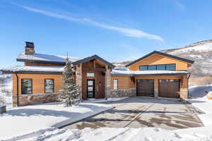 Modern home with stone siding, concrete driveway, a chimney, and an attached garage