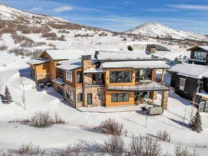 Snow covered house featuring stone siding, a balcony, a mountain view, and a patio area