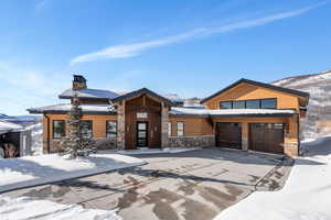 Modern home with concrete driveway, a chimney, stone siding, an attached garage, and a mountain view