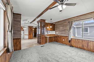 Kitchen featuring wood walls, light carpet, hanging light fixtures, beam ceiling, and ceiling fan