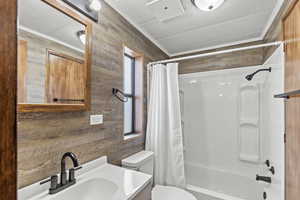Bathroom with a textured ceiling, vanity, ornamental molding, shower / tub combo with curtain, and wood walls