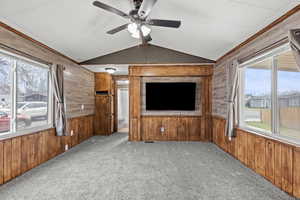 Unfurnished living room with light carpet, wood walls, a ceiling fan, and a residential view
