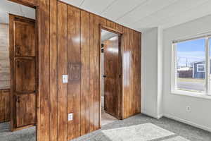 Unfurnished bedroom with light carpet and wood walls