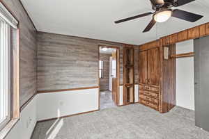Unfurnished bedroom featuring wood walls, light colored carpet, a ceiling fan, and a closet