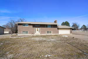 Raised ranch featuring brick siding, a chimney, driveway, and an attached garage