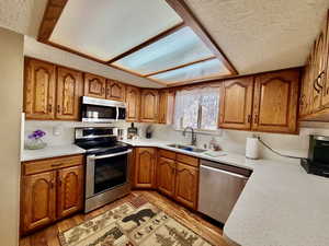 Kitchen featuring wood finish cabinetry, stainless steel appliances, light stone counters, and a textured ceiling