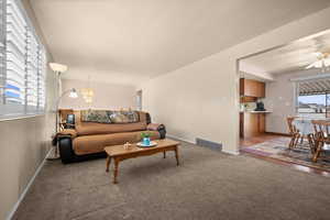 Living area featuring suspended lighting, dark carpet, and a ceiling fan