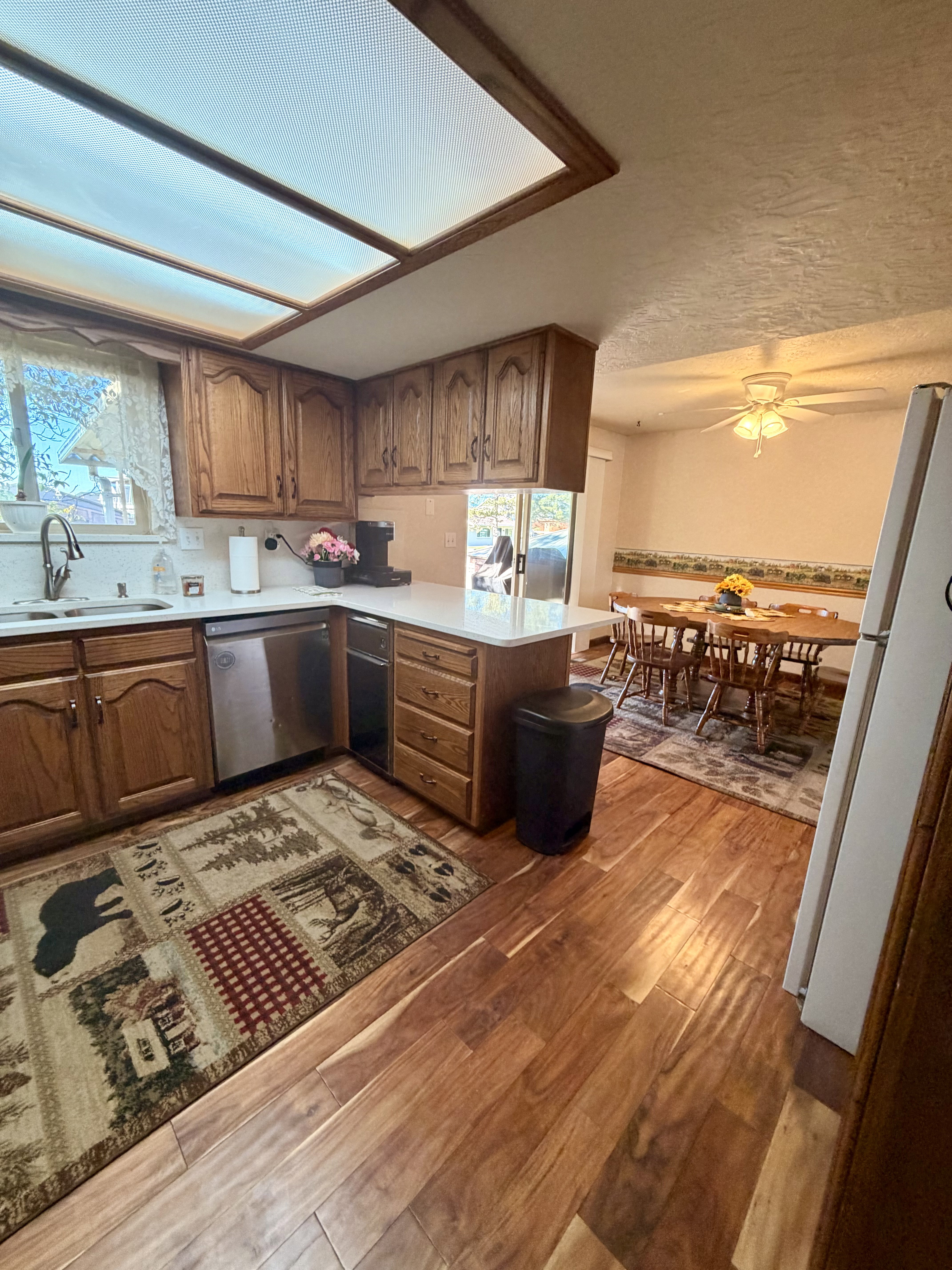 Kitchen featuring wood-finish flooring, oak cabinetry, white countertops, and a stainless steel dishwasher