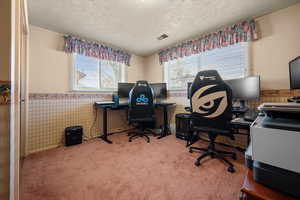 Carpeted office space with wallpapered walls, wainscoting, and a textured ceiling