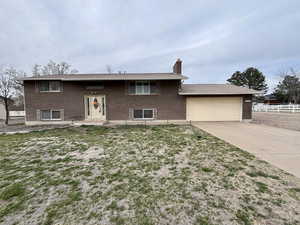Bi-level home featuring brick siding, driveway, a chimney, and a garage
