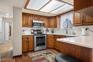 Kitchen with wood finish cabinets, stainless steel appliances, dark wood finished floors, and light stone countertops