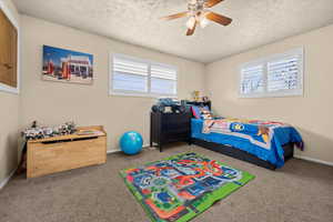 Carpeted bedroom featuring ceiling fan and a textured ceiling