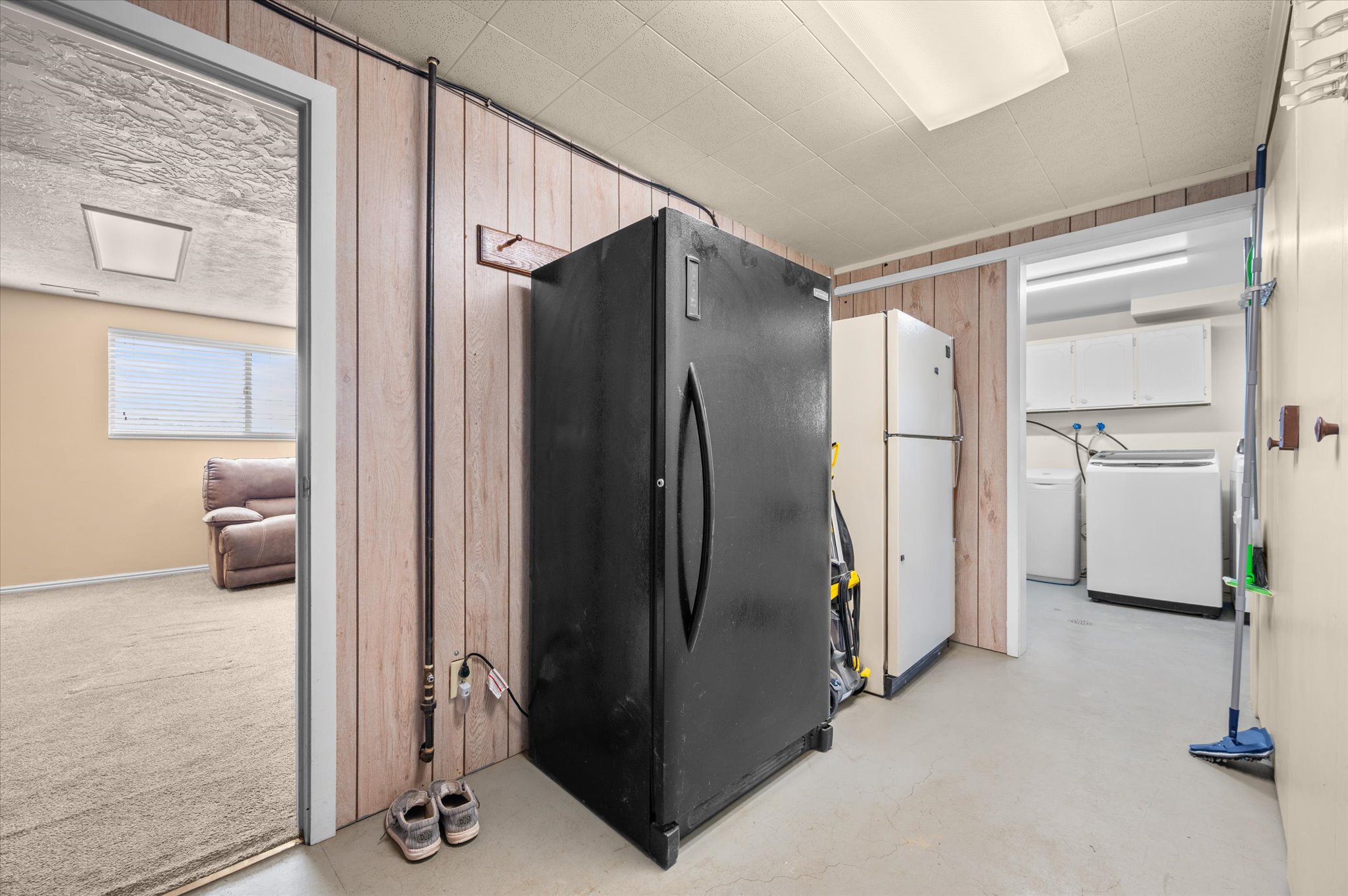 Kitchen with freestanding refrigerator, washer / dryer, finished concrete flooring, and wooden walls