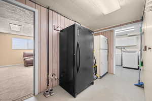 Kitchen with freestanding refrigerator, washer / dryer, finished concrete flooring, and wooden walls