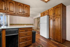 Kitchen featuring wood finish cabinetry, freestanding refrigerator, a textured ceiling, dark wood-style flooring, and light stone counters