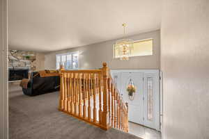 Carpeted foyer entrance with a chandelier and a stone fireplace