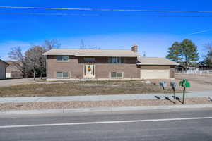 Raised ranch featuring a chimney, driveway, brick siding, and a garage