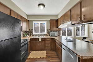 Kitchen featuring black appliances, a peninsula with lots of countertop space, plenty of natural light, light countertops, and a textured ceiling