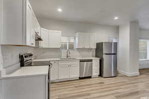 Kitchen featuring stainless steel appliances, white cabinets, light wood-style flooring, recessed lighting, and light stone countertops