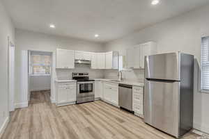 Kitchen with stainless steel appliances, white cabinets, light countertops, light wood finished floors, and recessed lighting