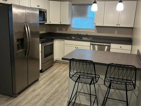 Kitchen with stainless steel appliances, a kitchen breakfast bar, a textured ceiling, hanging light fixtures, and dark countertops