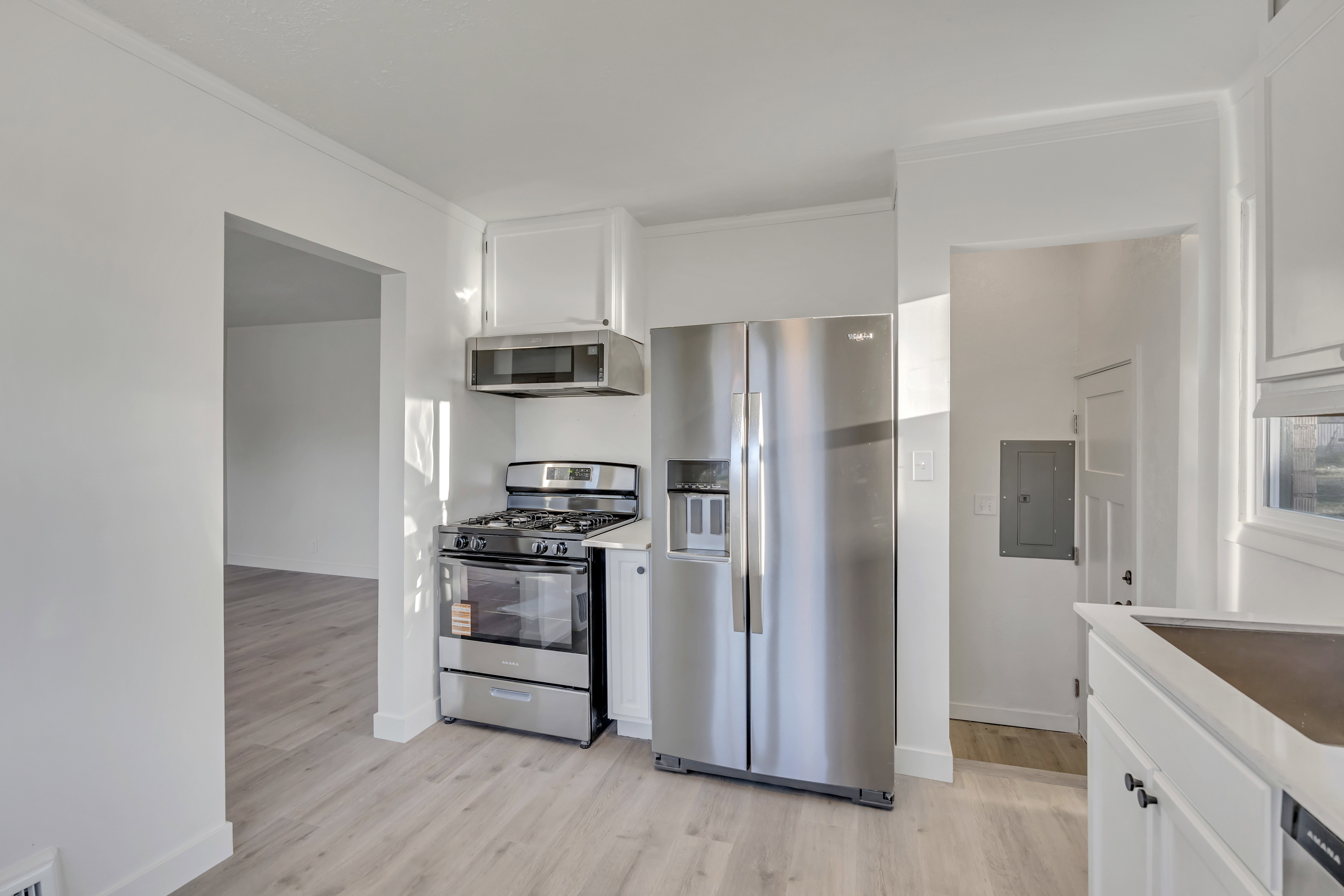 Kitchen featuring stainless steel appliances, white cabinetry, light wood finished floors, crown molding, and electric panel