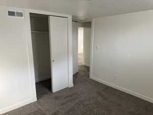 Unfurnished bedroom with a textured ceiling, dark carpet, and a closet