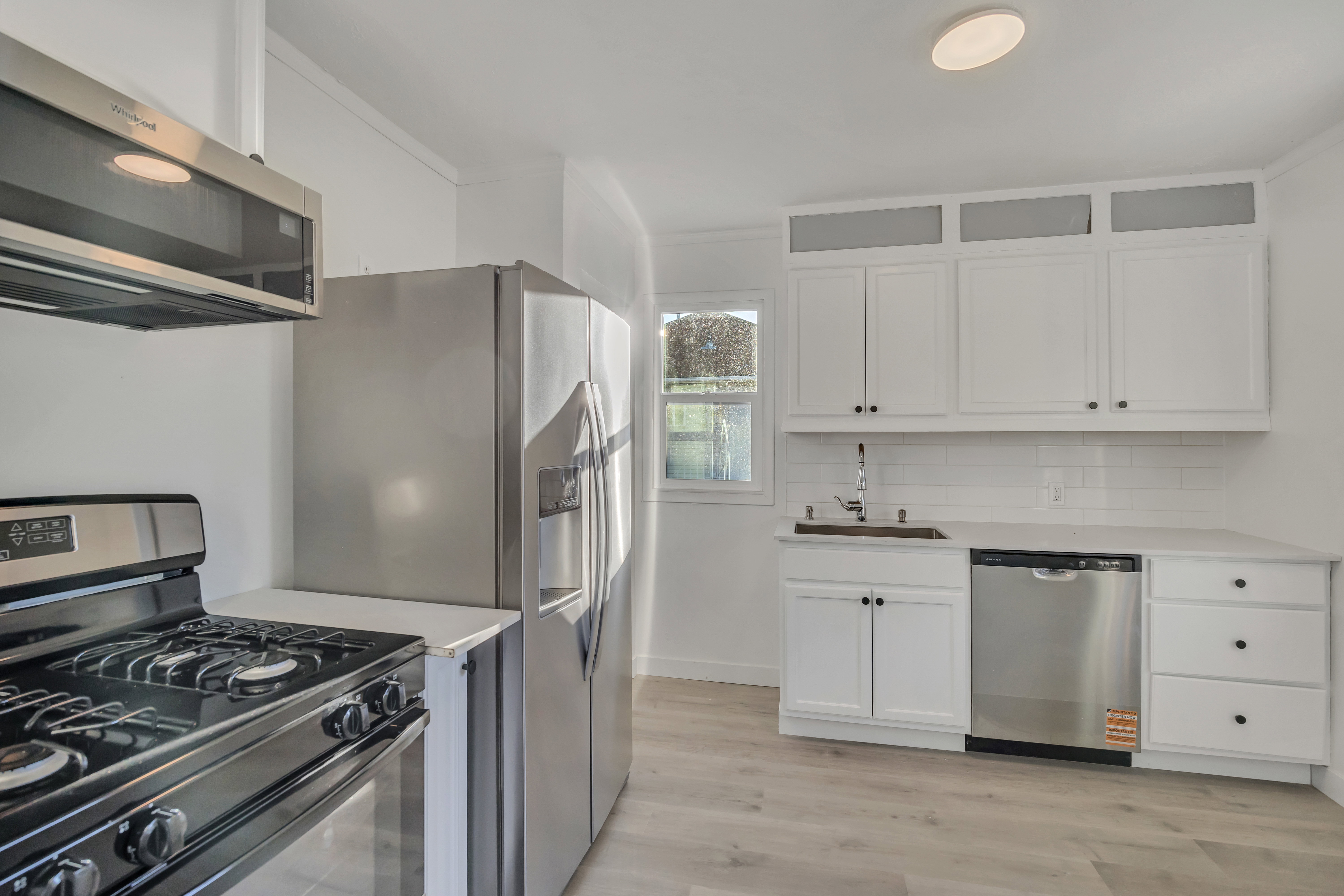 Kitchen featuring stainless steel appliances, white cabinets, light wood finished floors, crown molding, and tasteful backsplash