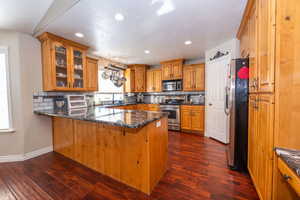 Kitchen featuring wood finish cabinetry, backsplash, a peninsula, dark stone counters, and stainless steel appliances