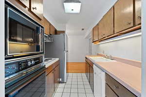 Kitchen with white appliances, wood finish cabinetry, light countertops, light tile patterned floors, and exhaust hood
