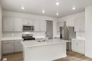 Kitchen with stainless steel appliances, light wood-style floors, a kitchen island with sink, light stone countertops, and recessed lighting