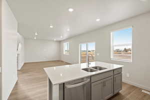 Kitchen featuring stainless steel dishwasher, a kitchen island with sink, light wood-style flooring, open floor plan, and light stone counters