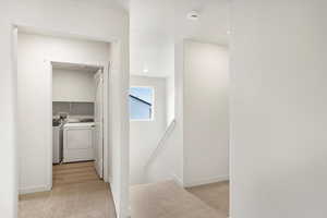 Hallway with light colored carpet, independent washer and dryer, and an upstairs landing