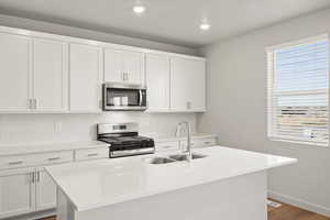 **DISCLAIMER** Interior package & colors may vary. Kitchen with stainless steel appliances, white cabinets, tasteful backsplash, light stone counters, and a center island with sink