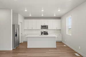 **DISLCAIMER** Interior package & colors may vary. Kitchen with white cabinets, stainless steel appliances, light wood-style flooring, an island with sink, and recessed lighting